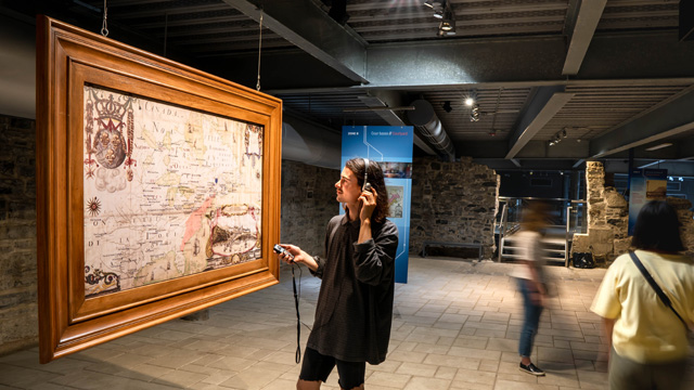 A visitor listening to an audio guide while looking at a giant map.