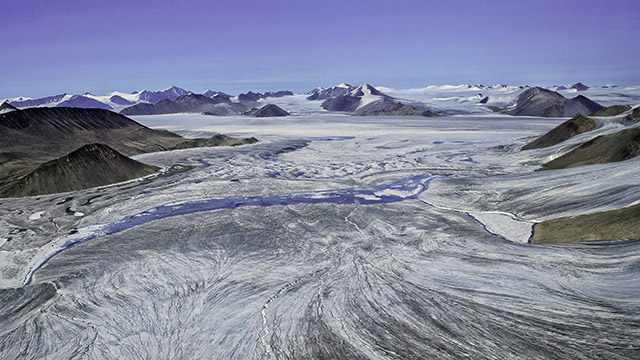 Aerial view of a massive glacier, with mountains in the distance. 