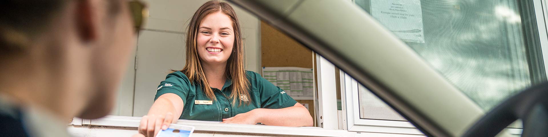 Une employée de Parcs Canada donne une brochure de renseignements aux visiteurs au kiosque d’entrée du terrain de camping de Cavendish. Parc national de l’Île-du-Prince-Édouard.